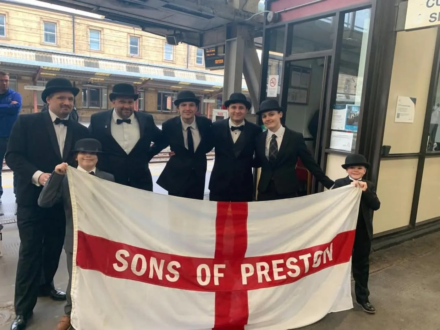 Preston supporters in bowlers with a Sons of Preston flag at a station on Gentry Day.