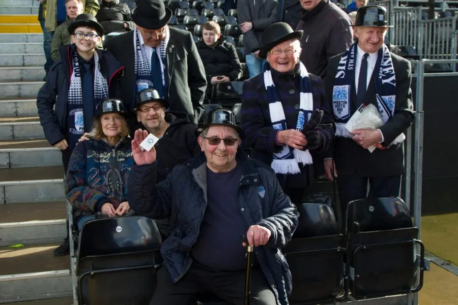Family and older supporters wearing bowlers and Preston scarves in the seats.